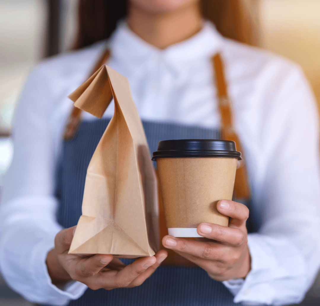 Un serveur tend la commande d'un client avec un sac en papier et une boisson à emporter